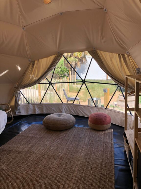 Interieur van een geodetische koepel met grote ramen, kussens en vloerkleed bij Wecamp Cabo de Gata, Spanje.