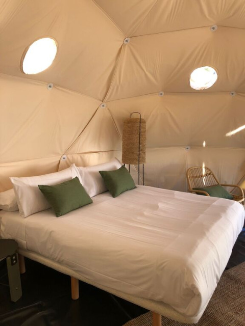 Slaapkamer met tweepersoonsbed, groene kussens en daglicht in een koepel bij Wecamp Cabo de Gata, Spanje.