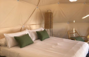 Slaapkamer met dubbel bed, groene kussens en natuurlijk licht in een dome bij Wecamp Cabo de Gata, Spanje.