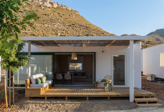 Mobil Home Family lodge met houten terras, zitgedeelte buiten en heuvelachtig uitzicht onder heldere lucht.