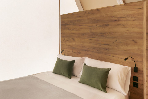Cama moderna con cabecero de madera y cojines verdes en tienda glamping familiar en Wecamp Cabo de Gata, España.