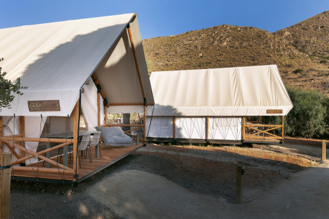 To safaritelte ved Glamping Family med træterrasse i naturen og bakker i baggrunden på en solrig dag.