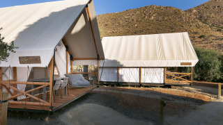 Twee safaritenten bij Glamping Family, voorzien van houten terras en gelegen tussen de heuvels in de zon.