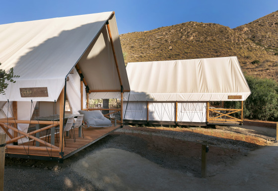 Deux tentes safari chez Glamping Family avec terrasses en bois, nichées près des collines sous un ciel bleu.