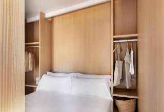 Dormitorio en la mobile home 'Couple Plus' en Wecamp San Sebastián, con paredes de madera y armario abierto.
