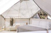 Interior of a safari bell tent with double bed, clothing rack, and natural light at Wecamp Santa Cristina.
