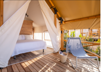 Tenda safari con letto matrimoniale e sedia lounge esterna a Glamping Couple, Wecamp Santa Cristina, Spagna.