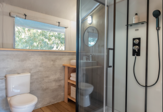 Moderne badkamer in een safaritent met houten vloer, glazen douche, toilet en raam met uitzicht.