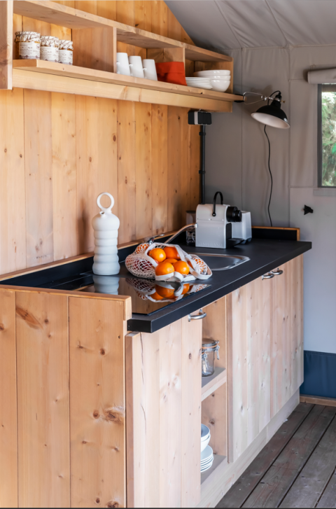 Keuken in safaritent met houten kasten, zwart werkblad, koffiemachine en net vol verse sinaasappels.