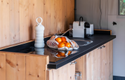 Safari tent kitchen with wood cabinets, black countertop, coffee maker, and netted bag of fresh oranges.