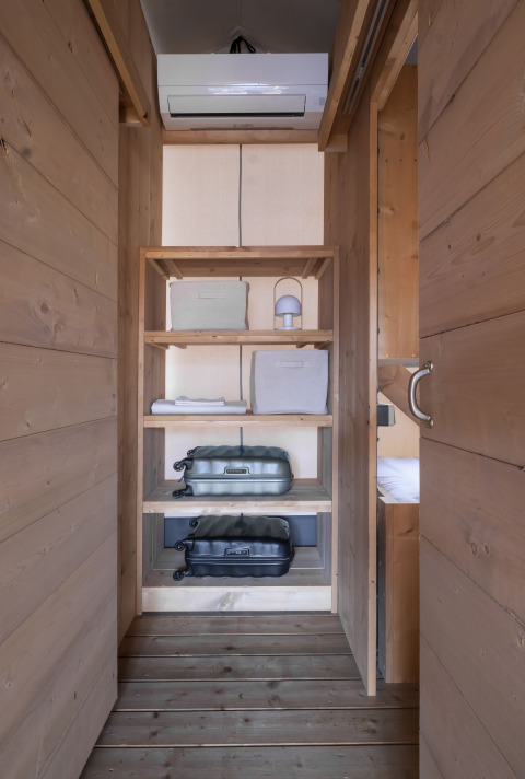 Houten open kast in een safaritent met koffers, opbergboxen en airconditioning bovenaan.