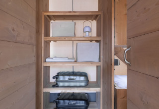 Houten open kast in een safaritent met koffers, opbergboxen en airconditioning bovenaan.