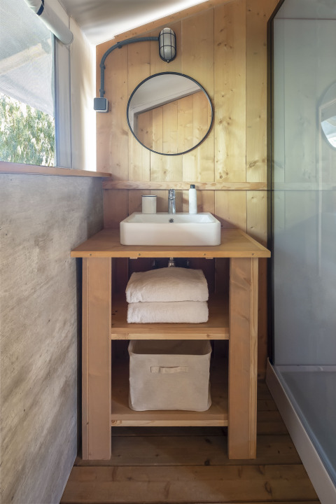 Badkamer van safaritent met houten wastafel, ronde spiegel, handdoeken en moderne minimalistische accenten.