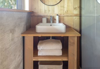 Baño en tienda safari con tocador de madera, espejo redondo, toallas y detalles modernos acogedores.