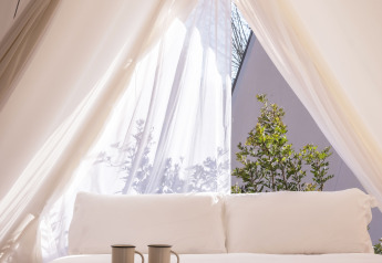 Bright safari tent bed with white linens and two mugs at Cabin Tent, Wecamp Santa Cristina, Spain.