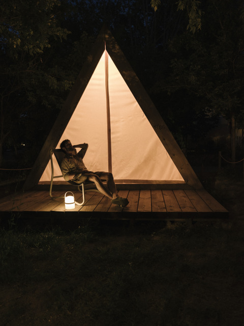Iemand ontspant 's nachts voor een driehoekige safaritent met lantaarn bij Wecamp Santa Cristina, Spanje.