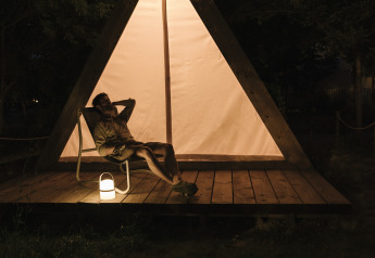 A person relaxes in front of a triangular safari tent at night with lantern at Wecamp Santa Cristina, Spain.