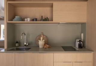 Moderne keuken met houten kasten, open planken, gootsteen en koffiemachine bij Wecamp Santa Cristina in Spanje.