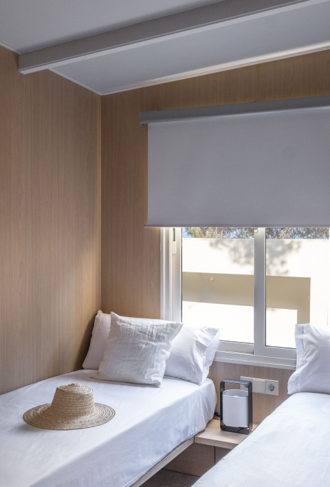 Kamer met twee eenpersoonsbedden, wit beddengoed, strohoed en raam in Mobil Home Family Plus in Spanje.