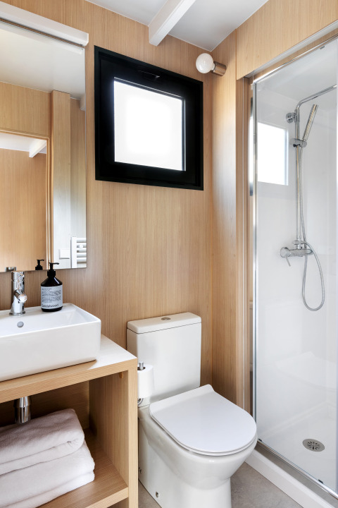 Baño moderno de lodge con ducha de vidrio, inodoro blanco, lavabo con toallas dobladas y paneles de madera.