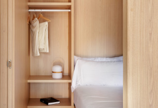Kleine slaapkamer met houten interieur, open kast, wit beddengoed en minimalistische inrichting in een lodge.