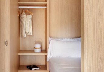 Petite chambre en bois avec penderie ouverte, lit blanc et décor minimaliste dans un lodge lumineux.