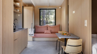 Interno di lodge moderno in legno chiaro con angolo cucina, tavolo da pranzo e divano vicino alla finestra.