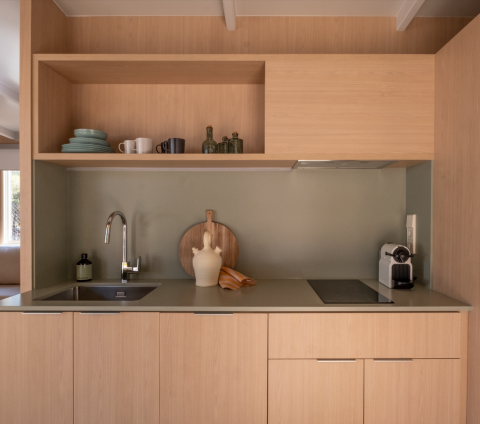 Cocina moderna con muebles de madera clara, estanterías abiertas y cafetera en Wecamp Santa Cristina, España.