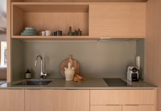 Cocina moderna con muebles de madera clara, estanterías abiertas y cafetera en Wecamp Santa Cristina, España.