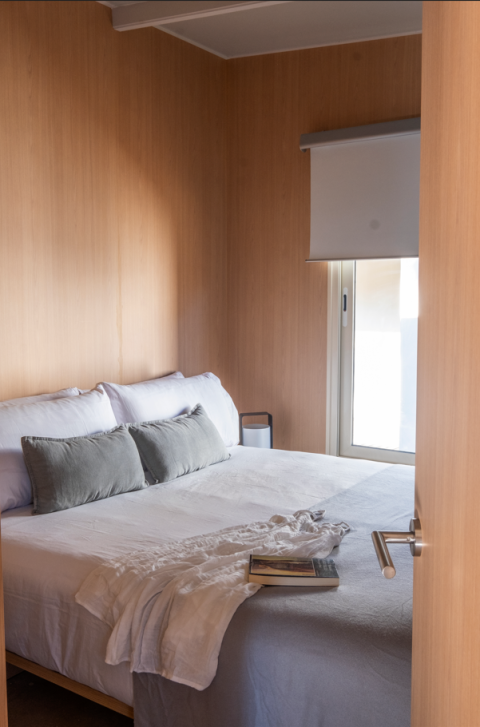 Dormitorio acogedor con cama doble, paredes de madera y ventana en Mobile Home Family, Wecamp Santa Cristina, España.