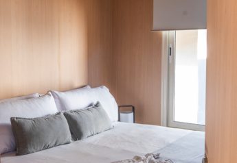 Chambre confortable avec lit double, murs en bois et fenêtre au Mobile Home Family, Wecamp Santa Cristina, Espagne.
