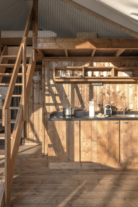 Interieur van de Lodge Family Duplex safaritent met houten keuken en slaapzolder bij Wecamp Santa Cristina.