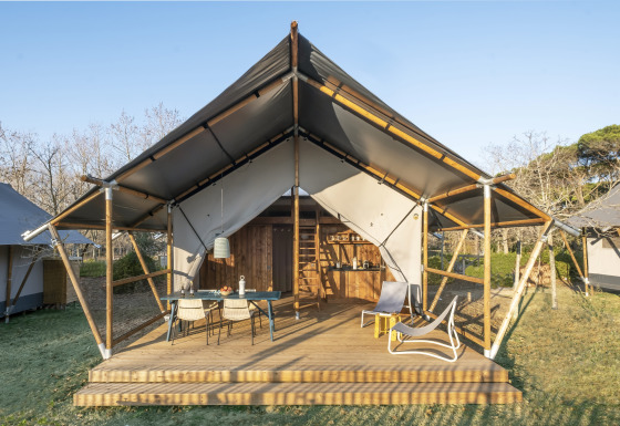 Lodge Family Duplex safaritent met houten veranda en buitenzitje in een natuurlijke, zonnige omgeving.