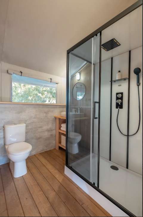 Moderne badkamer in safaritent met houten vloer, douche, toilet en raam bij Wecamp Santa Cristina.