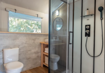 Bagno moderno in una tenda safari con pavimento in legno, doccia, wc e finestra a Wecamp Santa Cristina.