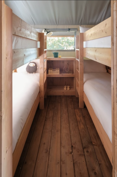 Gezellige slaapruimte met houten stapelbedden in een safaritent bij Wecamp Santa Cristina, Spanje.