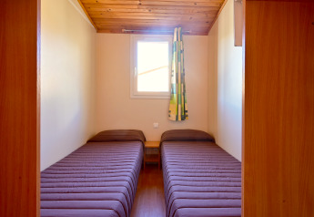 Zwei Einzelbetten mit brauner Bettwäsche im kompakten Zimmer des Mobile Home Basic Family, Wecamp Pedraforca, Spanien.