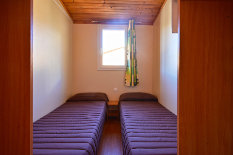 Dos camas individuales con ropa de cama marrón en una habitación pequeña de Mobile Home Basic Family, Wecamp Pedraforca, España.