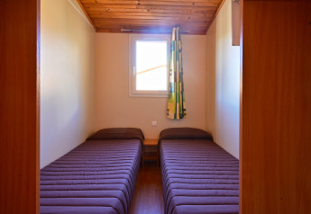 Dos camas individuales con ropa de cama marrón en una habitación pequeña de Mobile Home Basic Family, Wecamp Pedraforca, España.