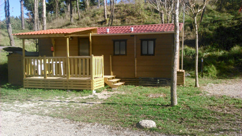 Mobile Home Basic Family au Wecamp Pedraforca en Espagne, avec terrasse en bois entourée d’arbres et nature.
