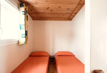 Camera luminosa con due letti singoli, coperte arancioni e soffitto in legno al Mobile Home Basic Family di Wecamp Pedraforca.