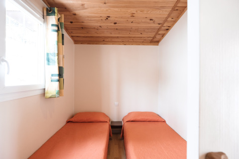 Lyst værelse med to enkeltsenge, orange sengetøj og træloft i Mobile Home Basic Family på Wecamp Pedraforca.