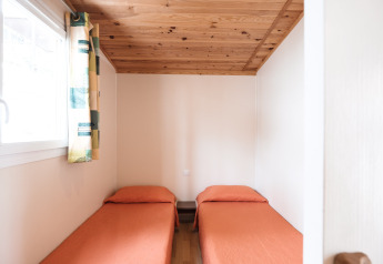 Habitación luminosa con dos camas individuales, ropa de cama naranja y techo de madera en Mobile Home Basic Family, Wecamp Pedraforca.