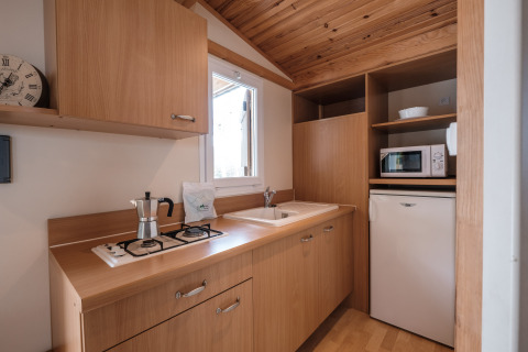 Area cucina della Mobile Home Basic Family al Wecamp Pedraforca in Spagna, con mobili in legno e elettrodomestici.