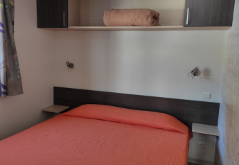Soveværelse i Mobile Home Basic Family+ Panoramic med orange sengetæppe på Wecamp Pedraforca i Spanien.