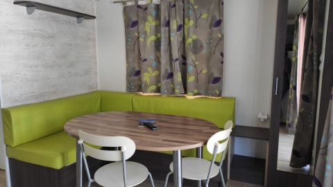 Eethoek van de Mobile Home Basic Family+ Panoramic met groene zitbanken en tafel bij Wecamp Pedraforca.