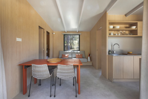 Lichte, moderne lodge met eettafel, keuken, zitbank en houten wanden met een groot raam achteraan.