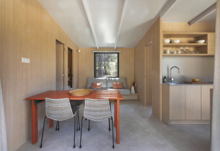 Lichte, moderne lodge met eettafel, keuken, zitbank en houten wanden met een groot raam achteraan.