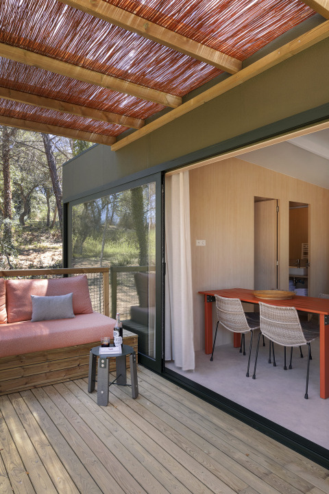 Terras van een moderne lodge met houten vloer, zitbank, eettafel en uitzicht op het bos.
