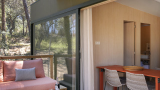 Terras van een moderne lodge met houten vloer, zitbank, eettafel en uitzicht op het bos.